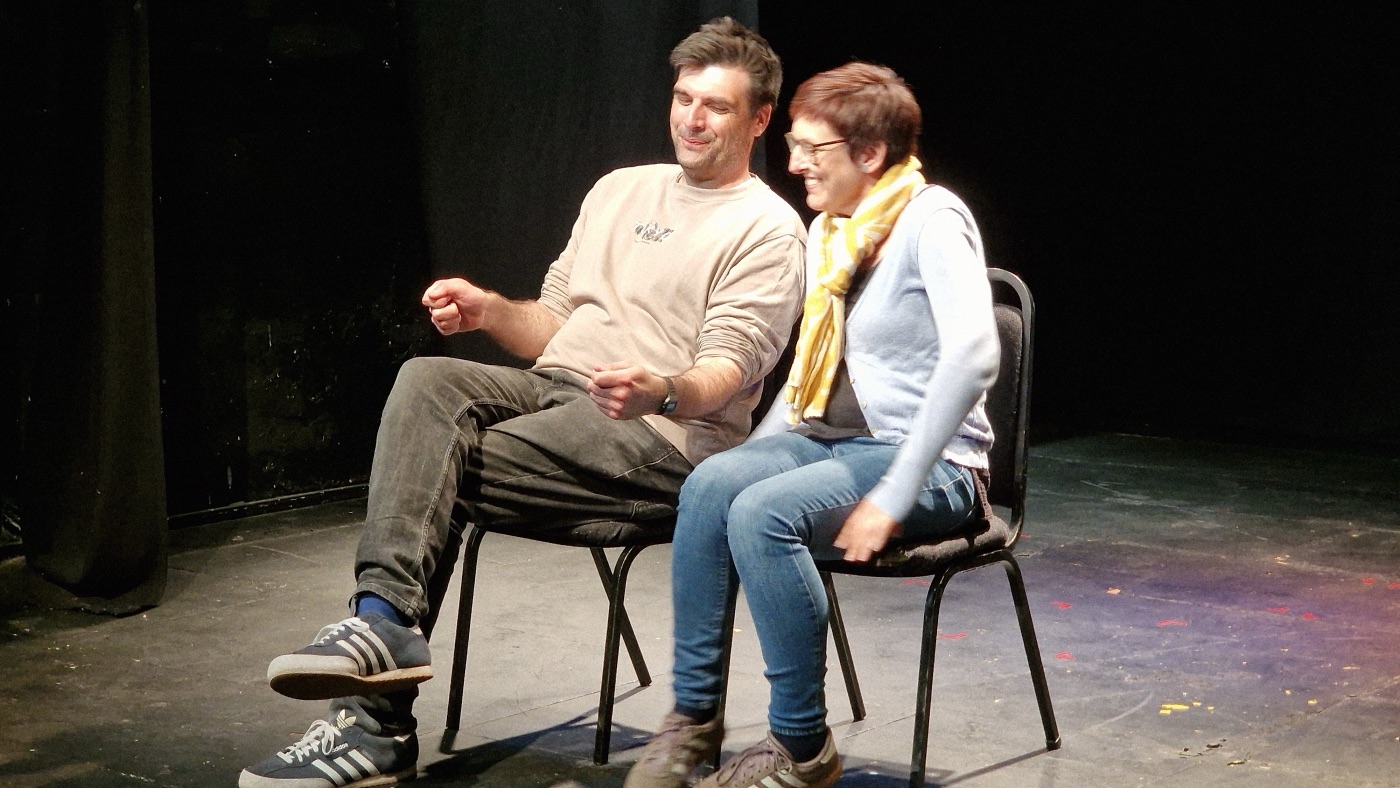 Two Dogface improvisers performing a seated scene on stage